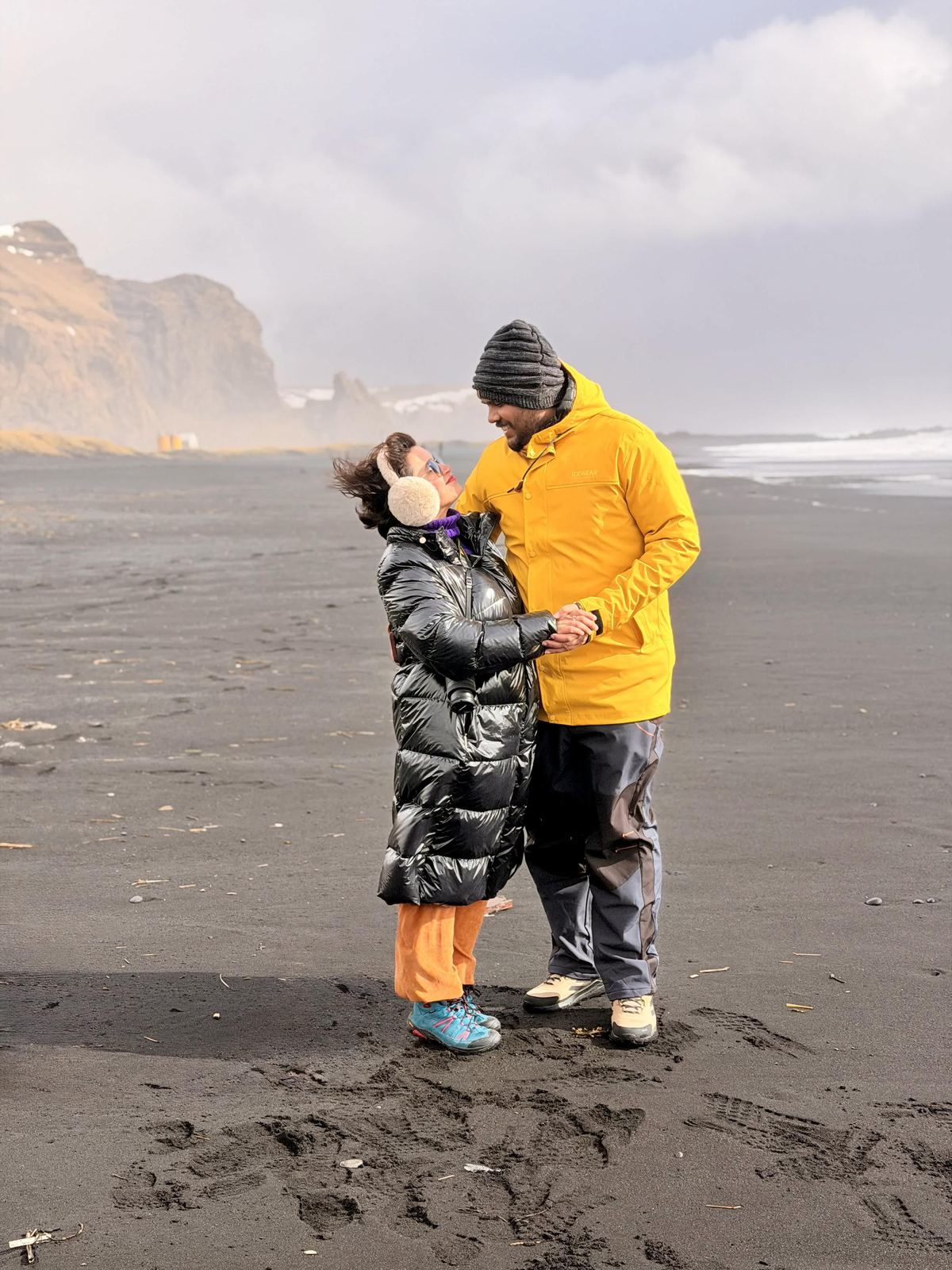 Sucheta and Utsav on the black beach, laughing, wind in hair